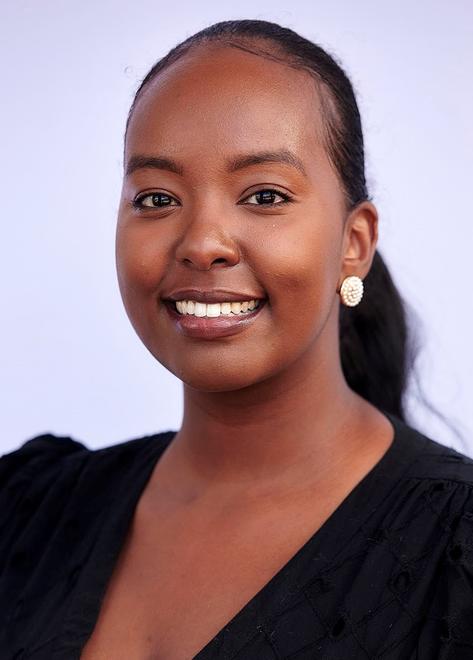 Asha Hassan, a smiling Black woman with dark brown skin, brown eyes, and slicked-back, black hair in a ponytail, wearing a professional blacktop and pearl earrings.